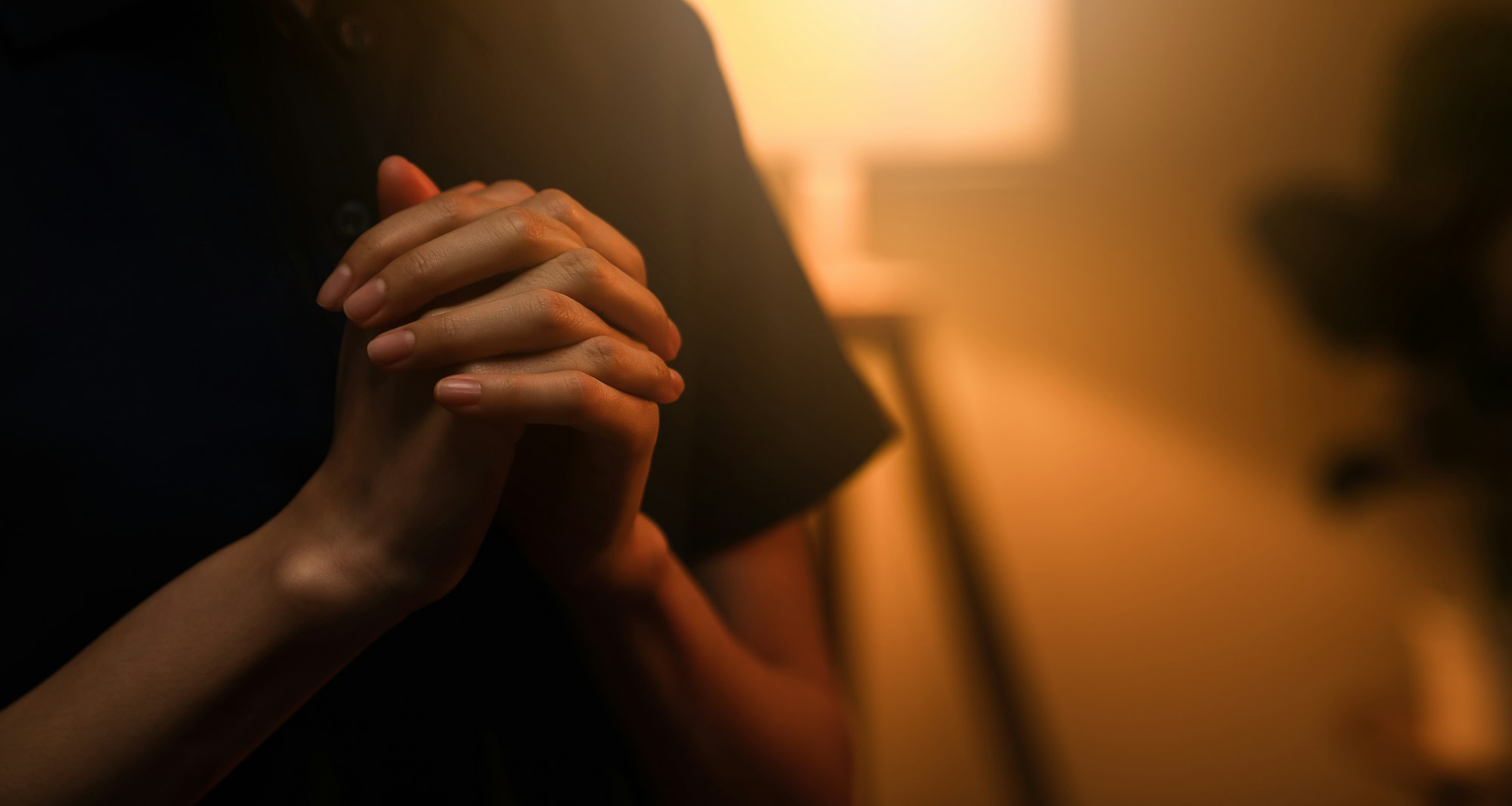 woman hand praying with magic light that flows through on orange bokeh background.