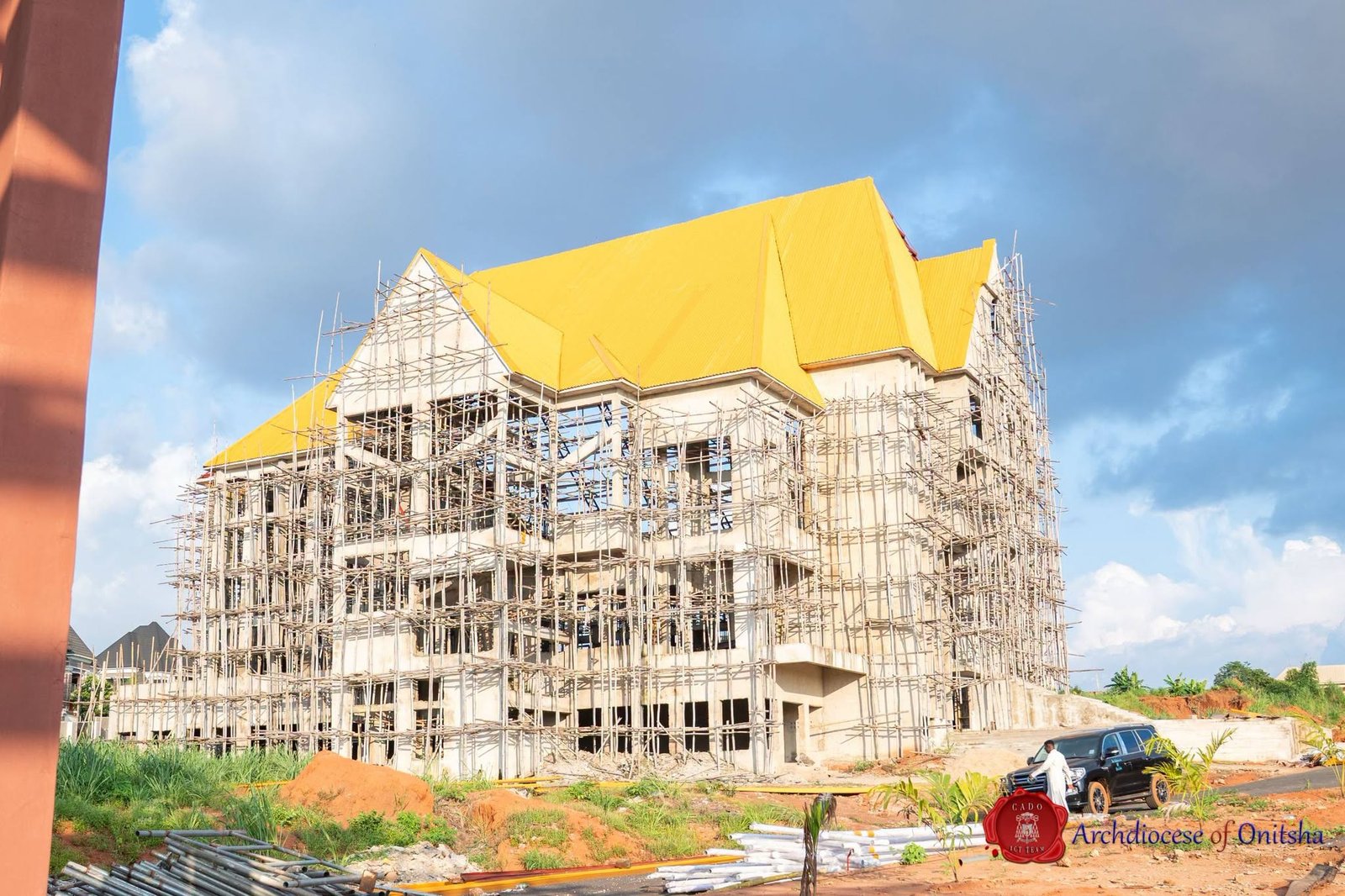 Campus building with golden roof rising behind bamboo scaffolding at Shanahan University Onitsha