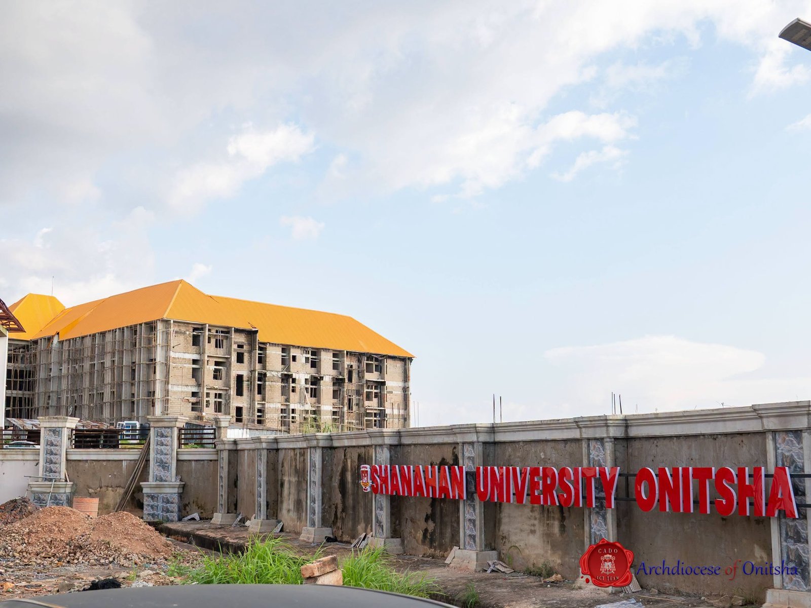 Shanahan University Onitsha signage on the campus perimeter wall with academic buildings behind
